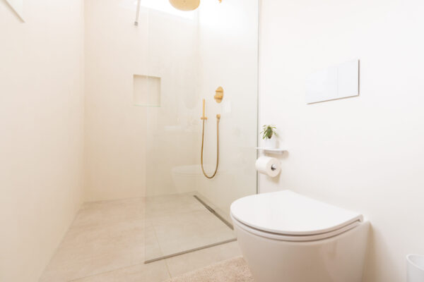 Fugenlose Duschwand mit obenliegender goldener Regenbrause und Wandarmatur, Basel – Malergenossenschaft Basel